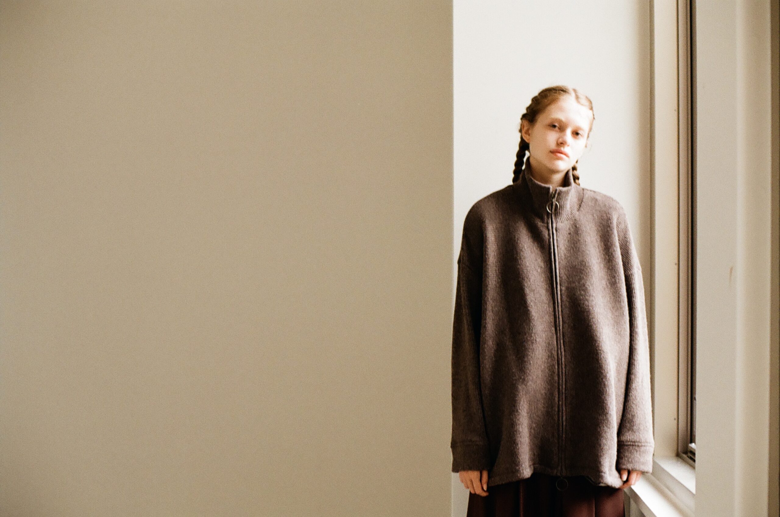 Model wearing an oversized zip knit beside a window in the Mochi 2026 Autumn Winter image look.