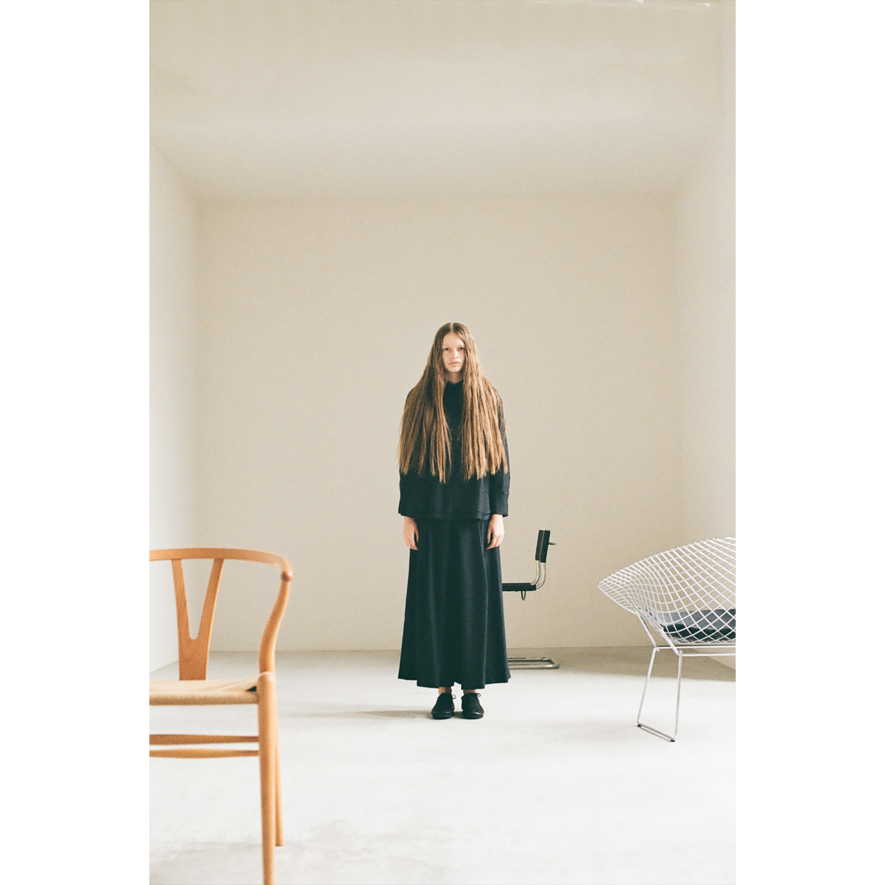 Mochi 2026 Autumn Winter image look 09 featuring a standing model in a black set-up surrounded by iconic furniture.