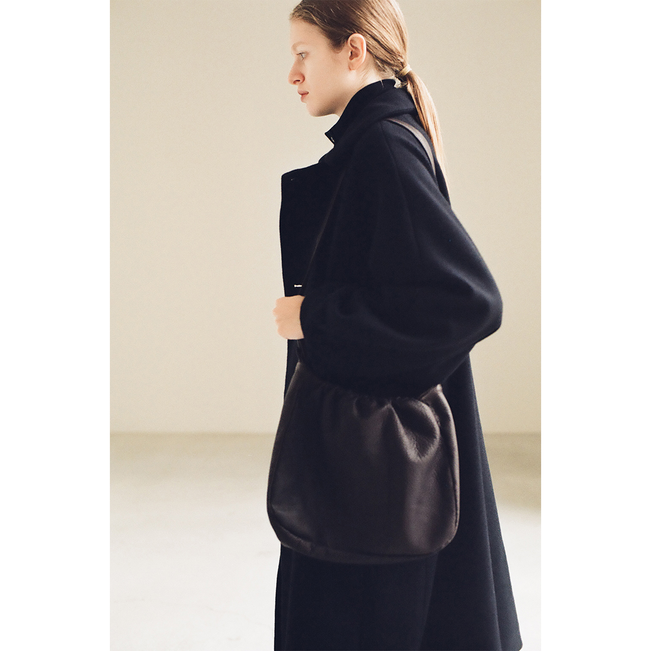Side view of a black coat with a deer leather bag in the Mochi 2026 Autumn Winter image look.